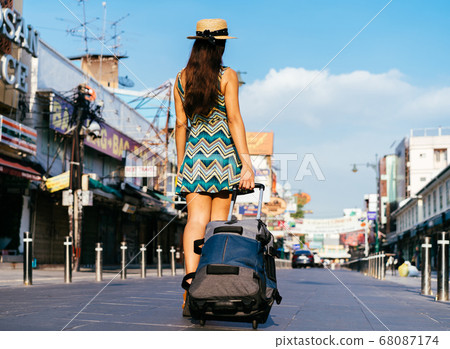 Young hispanic brunette woman pulling suitcase along pavement 68087174