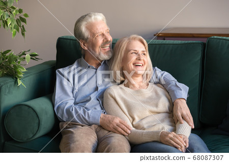 Happy hopeful old couple embracing resting on couch looking away 68087307