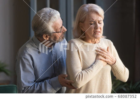 Worried elder husband helping wife touching chest having heart attack Worried elder husband helping wife touching chest having heart attack 68087352