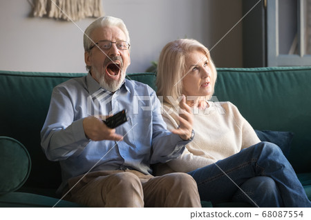 Bored middle-aged wife annoyed with senior husband watching sport tv 68087554