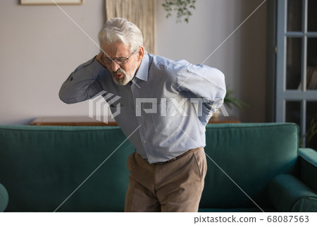 Upset senior man feeling back pain injury standing at home Upset senior man feeling back pain injury standing at home 68087563