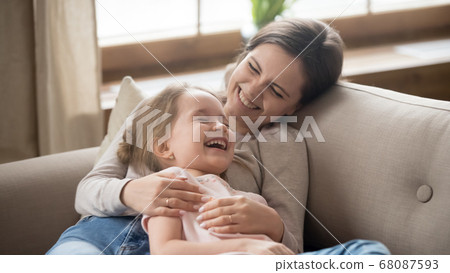 Happy mom embracing kid daughter laughing together lying on couch Happy mom embracing kid daughter laughing together lying on couch 68087593