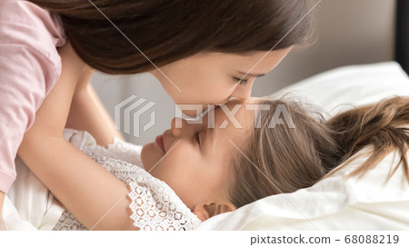 Loving mother kissing cute kid daughter waking up in morning 68088219
