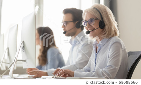 Smiling old female call center agent in headset consulting client Smiling old female call center agent in headset consulting client 68088660