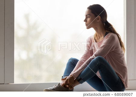 Sad pensive thoughtful girl sit on sill looking through window 68089007