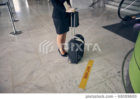 Elegant woman with travel suitcase waiting near check-in desk in airport Elegant woman with travel suitcase waiting near check-in desk in airport 68089600