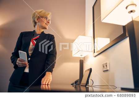 Beautiful businesswoman with smartphone standing in hotel room Beautiful businesswoman with smartphone standing in hotel room 68089893