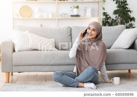 Cheerful arabic girl in headscarf talking on cellphone while relaxing at home 68089896