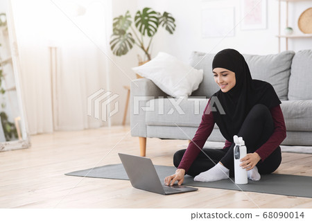 Online Fitness Tutorials. Sporty Muslim Woman Preparing For Home Workout, Using Laptop 68090014