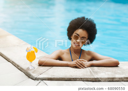 Hot African American lady relaxing in pool with tropical summer drink, copy space 68090550