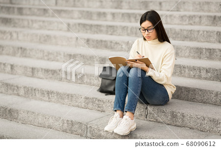 Girl writing in her diary, sitting on the gray stairs 68090612