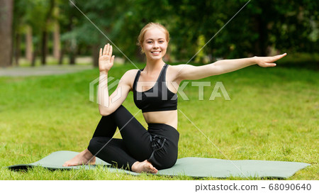 Pretty young woman twisting her body during outdoor yoga practice at park Pretty young woman twisting her body during outdoor yoga practice at park 68090640