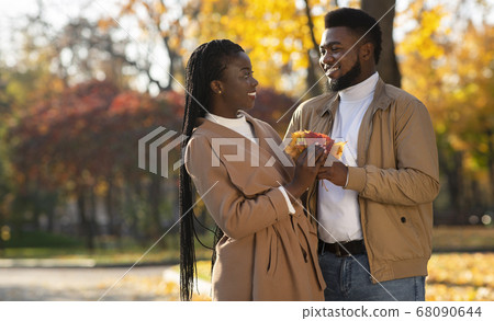 Romantic afro couple with bunch of leaves on date in park Romantic afro couple with bunch of leaves on date in park 68090644