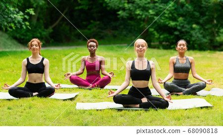 Outdoor yoga class. Group of diverse girls doing breathing exercises or meditation in nature Outdoor yoga class. Group of diverse girls doing breathing exercises or meditation in nature 68090818