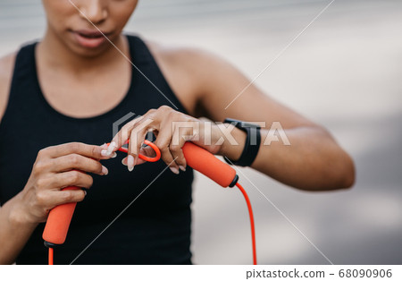 Adjustment of sports equipment. Girl in sportswear with fitness tracker adjusts skipping rope for workout Adjustment of sports equipment. Girl in sportswear with fitness tracker adjusts skipping rope for workout 68090906