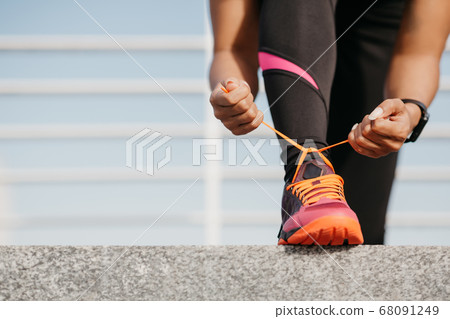 Start of day and workout. African american girl with fitness tracker in trendy sportswear tying shoelaces on bright sneakers Start of day and workout. African american girl with fitness tracker in trendy sportswear tying shoelaces on bright sneakers 68091249