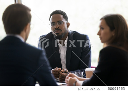 Serious african businessman listens speaker during group meeting in boardroom Serious african businessman listens speaker during group meeting in boardroom 68091663