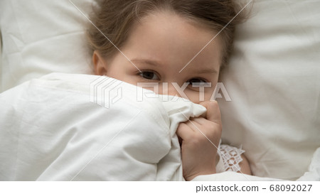 Cute kid girl looking at camera under blanket in bed Cute kid girl looking at camera under blanket in bed 68092027