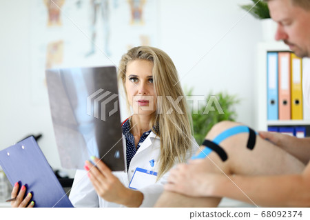 Doctor woman with examines an x-ray of leg next to patient sits. Doctor woman with examines an x-ray of leg next to patient sits. 68092374