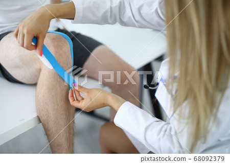 Nurse should glue kinesio tape on athlete's injured knee Nurse should glue kinesio tape on athlete's injured knee 68092379