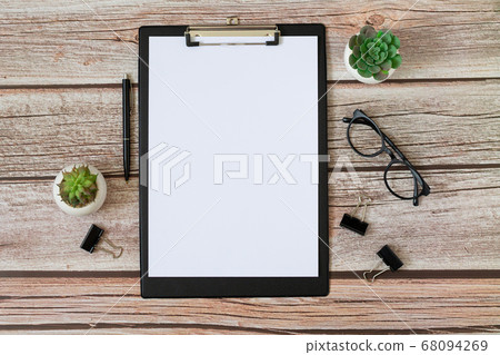 Wooden office desk table with clipboard, supplies, glasses and plants top view. Blank notebook page for text 68094269