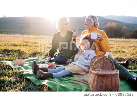 Small girl with mother and grandmother having picnic in nature at sunset. Small girl with mother and grandmother having picnic in nature at sunset. 68095522