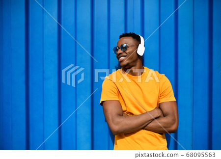 Young black man with headphones standing against blue background, black lives matter concept. Young black man with headphones standing against blue background, black lives matter concept. 68095563