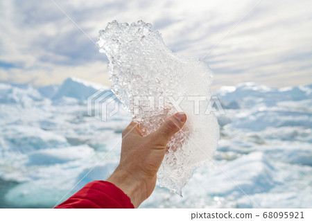 Global warming, climate change and Environmental protection concept with icebergs on Greenland. Hand holding melting ice by giant iceberg in Ilulissat icefjord on Greenland. Save the climate 68095921