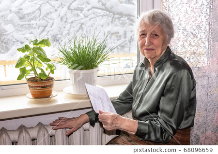 Woman holding cash in front of heating radiator. 68096659