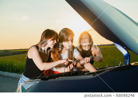 Three young women fix car at road trip Three young women fix car at road trip 68098246
