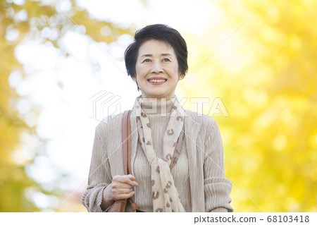Senior woman walking along a row of ginkgo trees Senior woman walking along a row of ginkgo trees 68103418
