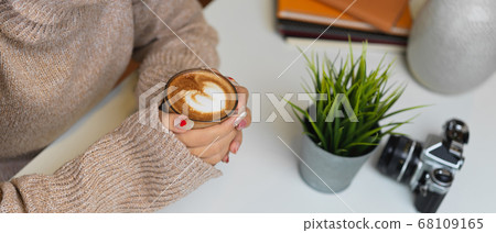 Side view of female in sweater hands holding a cup Side view of female in sweater hands holding a cup 68109165