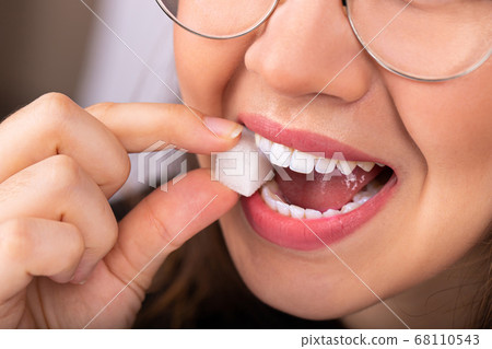 Beautiful woman mouth with big white teeth bites on a white sugar cube 68110543