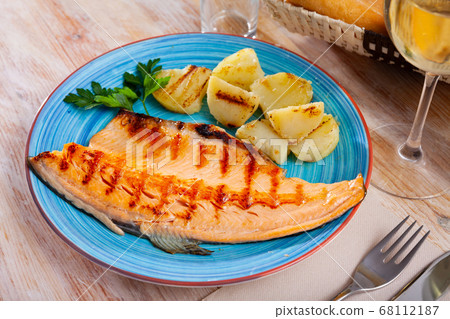 Fried trout fillet with baked potatoes on blue plate Fried trout fillet with baked potatoes on blue plate 68112187