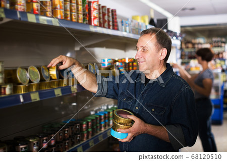 Pensioner selecting preserves at store Pensioner selecting preserves at store 68120510