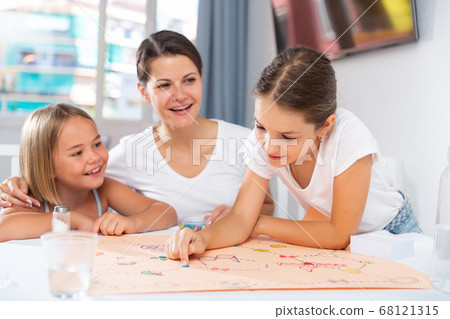 Mom with two daughters play board game at the table Mom with two daughters play board game at the table 68121315