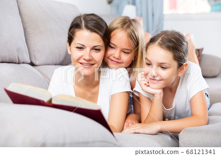 Mom reads tales for her daughters lying on sofa Mom reads tales for her daughters lying on sofa 68121341
