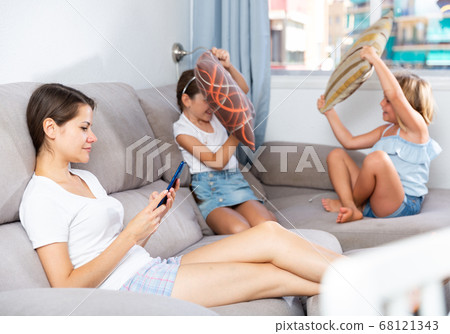 Woman using phone while daughters pillow fighting Woman using phone while daughters pillow fighting 68121343