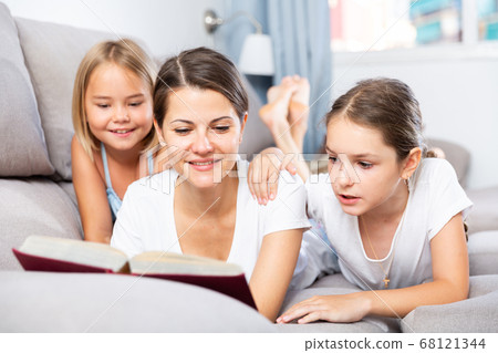 Woman reading book to daughters on sofa Woman reading book to daughters on sofa 68121344