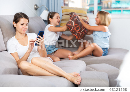 Woman using phone while daughters pillow fighting Woman using phone while daughters pillow fighting 68121368