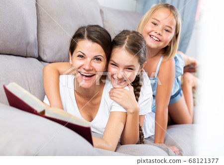 Woman and two daughters resting on sofa 68121377