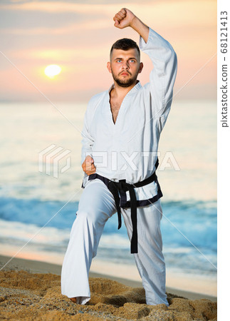 Guy doing karate poses at sunset sea shore 68121413