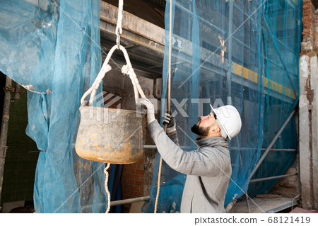 Man raising bucket with construction mortar on rope 68121419