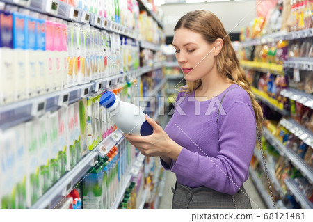 Portrait of smiling woman holding bottle with fresh milk in grocery shop 68121481