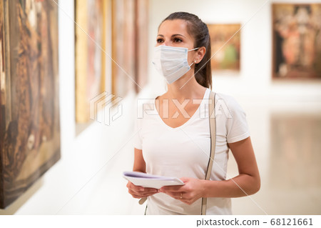 Woman in mask observing artworks in museum Woman in mask observing artworks in museum 68121661
