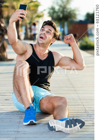 Cheerful sporty man showing biceps and taking selfie on beach fitness station Cheerful sporty man showing biceps and taking selfie on beach fitness station 68121760