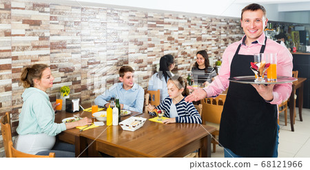 Smiling male waiter warmly welcoming guests to family cafe Smiling male waiter warmly welcoming guests to family cafe 68121966