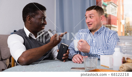 Men enjoying conversation at home, using phone 68122218