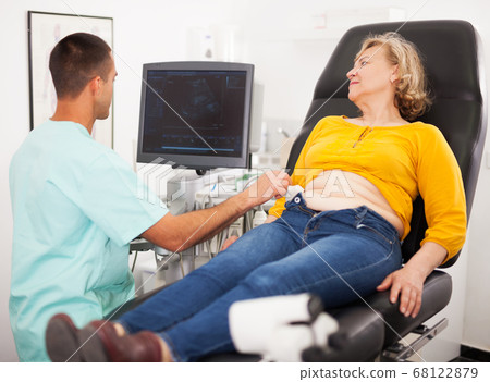 doctor examines a mature woman at abdomen with ultrasound doctor examines a mature woman at abdomen with ultrasound 68122879