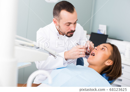Dentist is treating patient which is sitting in dental chair in clinic Dentist is treating patient which is sitting in dental chair in clinic 68123625